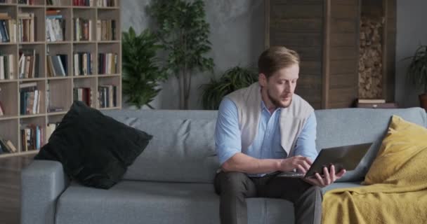 Homem de negócios europeu confiante trabalhando remotamente usar laptop no sofá na acolhedora sala de estar — Vídeo de Stock