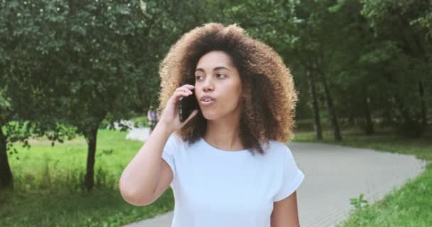 Glimlachende Afro-Amerikaanse moderne casual dame gesticuleer emotioneel praten over de telefoon — Stockvideo
