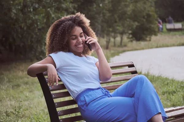 Una hermosa mujer afroamericana habla por teléfono con amigos o colegas, se relaja, disfruta de la comunicación remota. —  Fotos de Stock