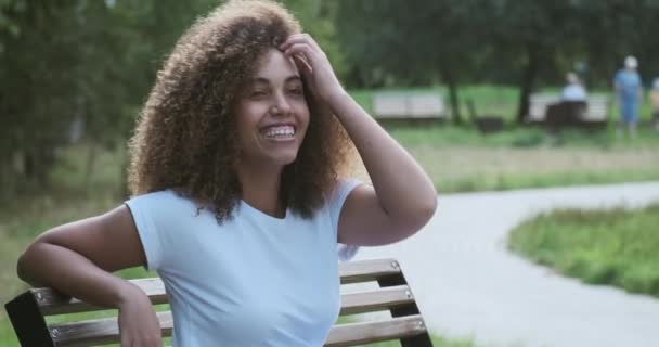 Porträtt av avslappnad ung leende afroamerikansk kvinna avkopplande poserar på sommar park bänk — Stockvideo