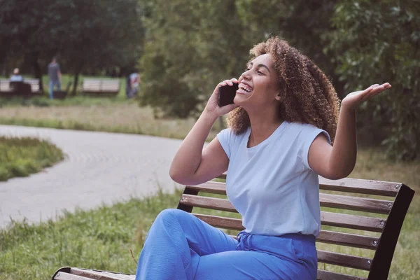 Sonriendo afroamericana moderna dama casual gesticular emocionalmente hablando por teléfono —  Fotos de Stock