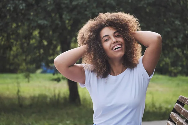 Retrato adorable sonriente mujer rizada afroamericana en camiseta casual blanca posando en el parque de verano —  Fotos de Stock