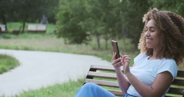 Feliz joven mujer africana negra pasar tiempo al aire libre utilizando su teléfono celular y tener la comunicación — Vídeo de stock