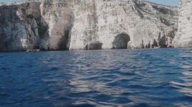 Mavi deniz dalgaları kayalık kayalıklarla kahverengi tepenin kenarını yendi.