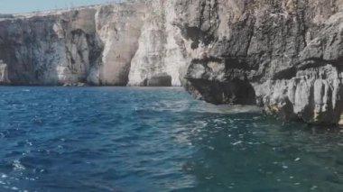 Mavi deniz dalgaları kayalık kayalıklarla kahverengi tepenin kenarını yendi.