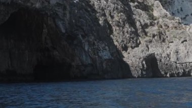 Mavi deniz dalgaları kayalık kayalıklarla kahverengi tepenin kenarını yendi.