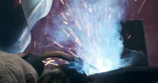 Male welder in uniform protective clothes, helmet, gloves welding metal part illuminated glow lights — Stock Video