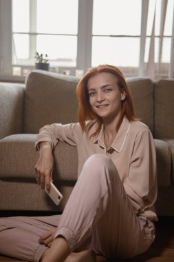 Beyaz, güzel, kızıl saçlı bir kadın. Odadaki kanepenin yanında oturuyor ve akıllı telefondan vuruyor ya da oynuyor..