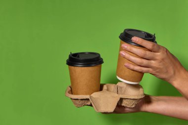 Yeşil arka planda yakın plan, kadınların elleri bir stantta kahve ile iki kağıt bardak tutuyor. Seninle kahve ya da çay. Bir fiyatına iki terfi, kahve teslimatı..