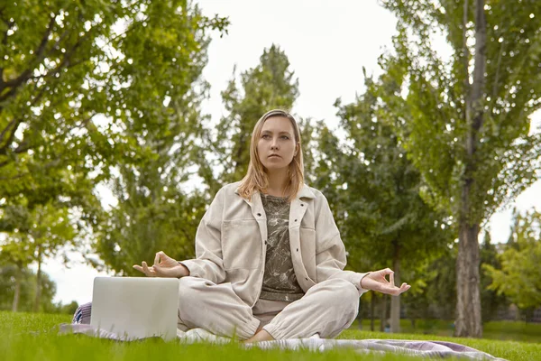 Woman sitting in lotus pose, crossed leg posture (Sukhasana) and meditating in a park. An attractive woman relieves stress by meditating in the park