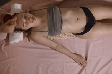 Güzel bir kadın sırtında çivilerle tahtada yatıyor. Acı yoluyla terapi, onun kabulüdür. Aşırı rahatlama ve kendini geliştirme yogası 