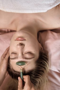 Genç ve güzel bir kadın sağlık merkezinde Gua Sha masajı yaptırıyor. Masör, kaplıca salonundaki genç ve güzel bir kızın kafasına masaj yapıyor. Makroyu kapat. 