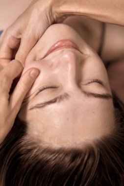 Genç ve güzel bir kadın, sağlık merkezinde kafa ve yüz masajı yaptırıyor. Masör, kaplıca salonundaki genç ve güzel bir kızın kafasına masaj yapıyor. Makroyu kapat. 