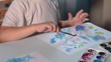 Odasındaki bir masada boyayla resim çizen bir çocuk. Yüksek kalitede FullHD görüntüsü olan bir çocuk odasındaki bir masada boyalarla resim çizer..