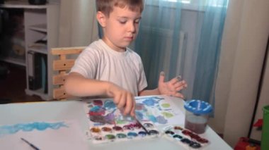Odasındaki bir masada boyayla resim çizen bir çocuk. Yüksek kalitede FullHD görüntüsü olan bir çocuk odasındaki bir masada boyalarla resim çizer..