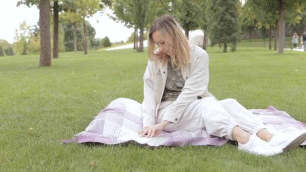 Student vrouw ontspant terwijl zitten op een deken in het park. — Stockvideo