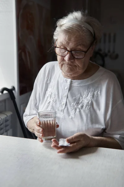 Uma mulher idosa toma um comprimido e bebe um copo de água — Fotografia de Stock