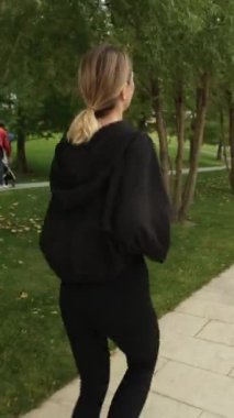 Siyah eşofmanlı bir kadın parkta spor yapıyor.