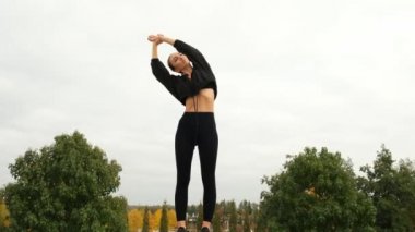 Siyah eşofmanlı bir kadın parkta spor yapıyor.