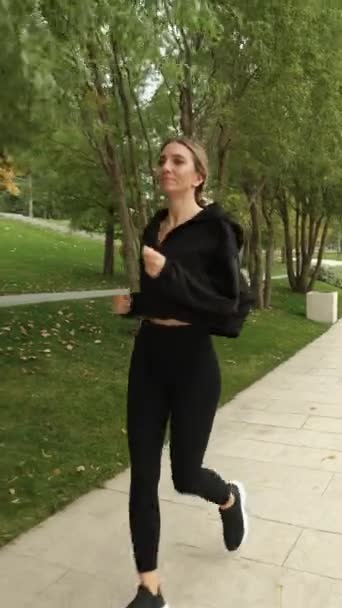 A woman in a black tracksuit does sports in the park — Stockvideo