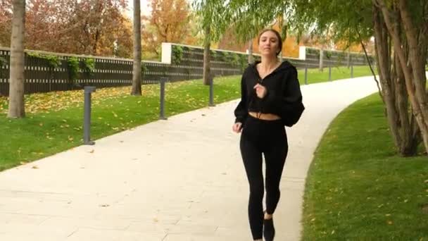 A woman in a black tracksuit does sports in the park — Stockvideo