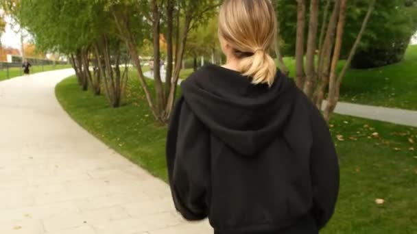 A woman in a black tracksuit does sports in the park — Stockvideo