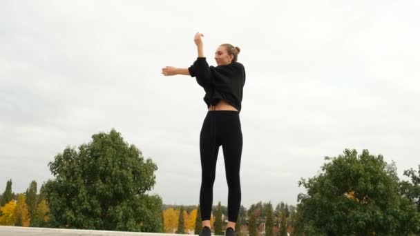 A woman in a black tracksuit does sports in the park — Stockvideo