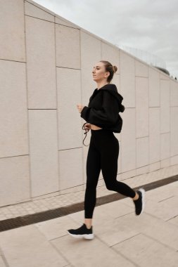 Siyah eşofmanlı bir kadın parkta spor yapıyor.