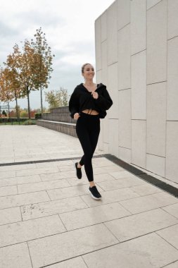 Siyah eşofmanlı bir kadın parkta spor yapıyor.