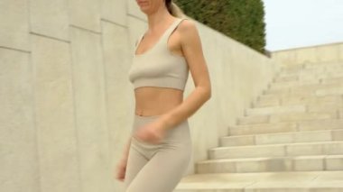Orta yaşlı sarışın, beyaz kadın atlet bej bluz giymiş ve tayt parkta spor yapıyor.