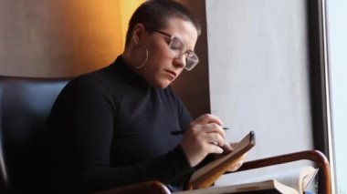 Bir kadın kafede oturuyor ve tablette çalışıyor..