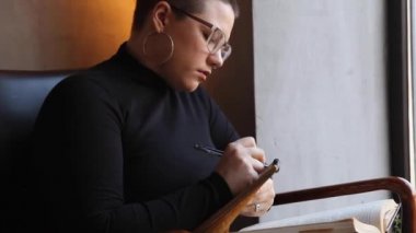 Bir kadın kafede oturuyor ve tablette çalışıyor..