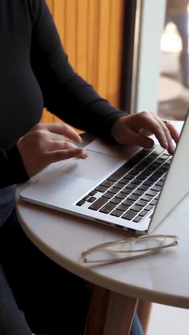 Uma mulher senta-se em um café e trabalha em um laptop. — Vídeo de Stock