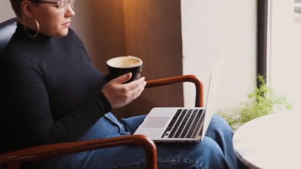 Een vrouw met een bril zit in een café en werkt op een laptop. — Stockvideo