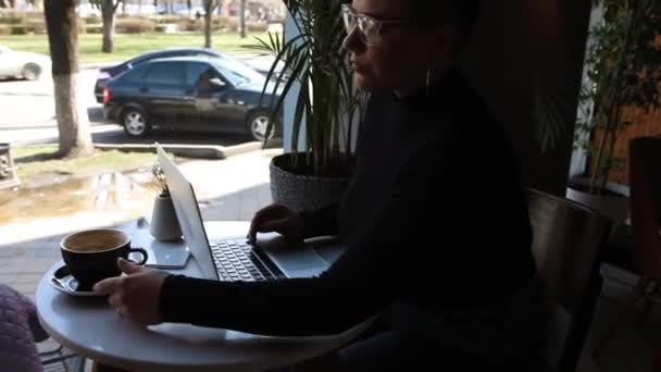 Uma mulher senta-se em um café e trabalha em um laptop. — Vídeo de Stock