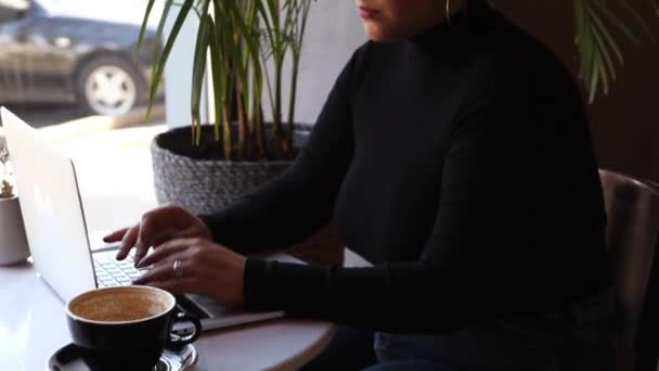 Una mujer se sienta en un café y trabaja en un portátil. — Vídeos de Stock