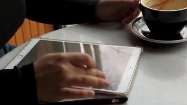 Una mujer se sienta en un café y trabaja en una tableta. — Vídeos de Stock