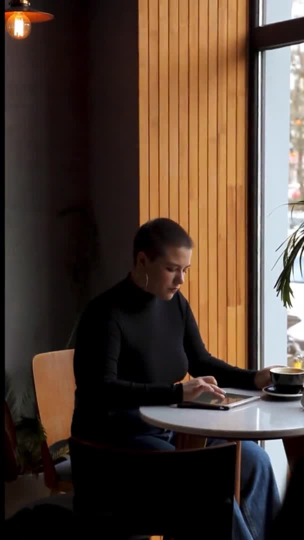 Uma mulher senta-se em um café e trabalha em um tablet. — Vídeo de Stock
