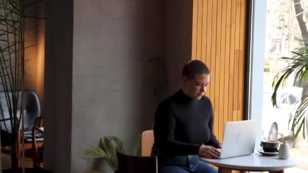 O femeie stă într-o cafenea și lucrează la un laptop . — Videoclip de stoc