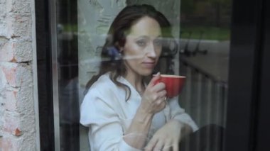 Pencerenin kenarında oturup kahve içen bir kadın.