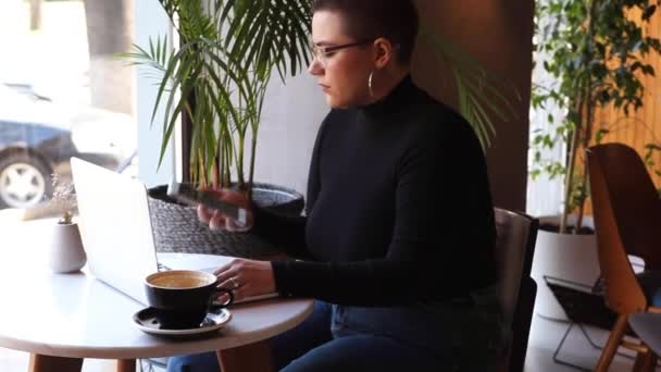 Una mujer se sienta en un café y trabaja en un portátil. — Vídeo de stock