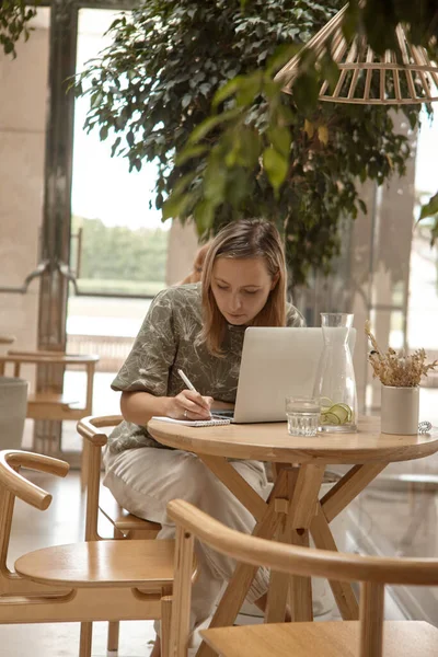 Uma mulher senta-se em um café e trabalha em um laptop — Fotografia de Stock