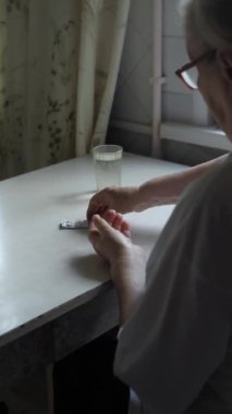 Yaşlı bir kadın tablet alır ve bir bardak su içer.