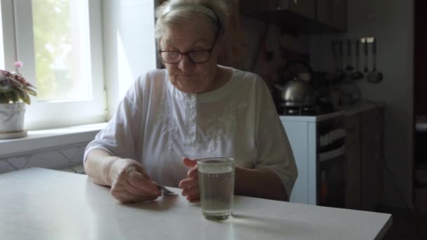 Пожилая женщина принимает таблетки и пьет стакан воды — стоковое видео