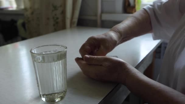 Uma mulher idosa toma um comprimido e bebe um copo de água — Vídeo de Stock