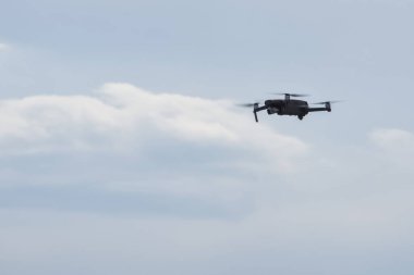 Küçük drone kuadkopteri bulutlu mavi gökyüzünün arka planında bir kamera ile uçar..