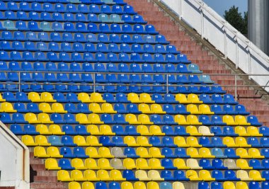Stadyumdaki taraftarlar tribünü. Futbol sahasındaki insanlar için mavi ve sarı koltuklu bir sürü sıra..