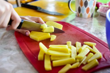 Mutfakta bir çocuk tahtada patates kesiyor. Evde kızarmış patates pişirmek..
