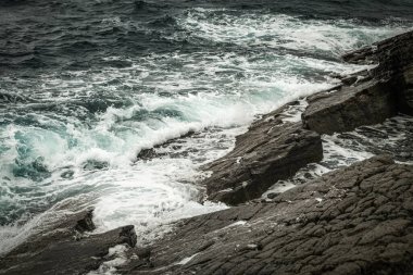 Su sıçratan ve köpüren deniz dalgaları kayalık taşların üzerinde süzülür..