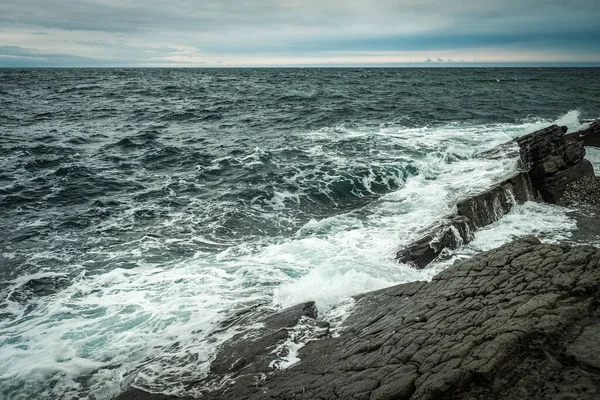 砕石と泡で波が岩の上を洗い — ストック写真